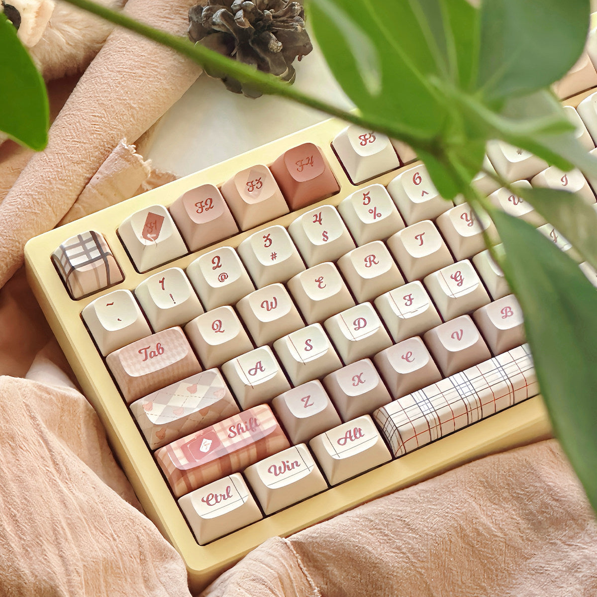 Pink and beige themed keyboard with decorative keycaps featuring plaid, floral, and cute icons, placed on a soft pink fabric surface
