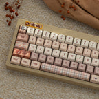 Close-up of a beige and pink autumn British style keycap set with plaid and heart patterns, featuring Cherry profile PBT material on a textured surface.