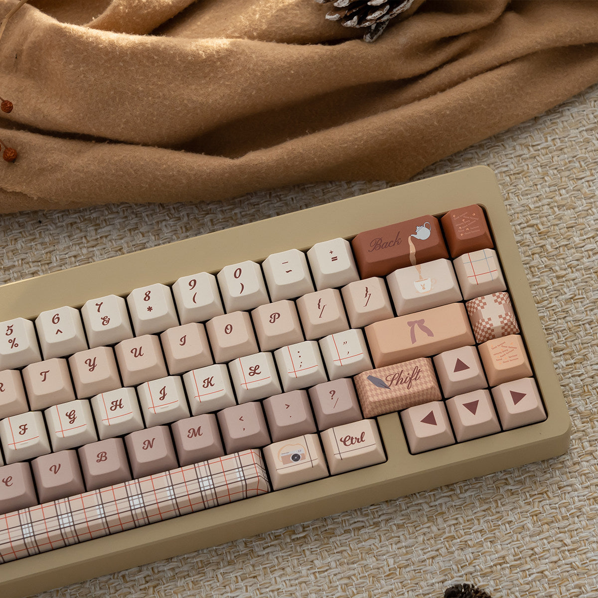 Arrangement of pastel pink and beige keycaps with cute illustrations and plaid designs, showcasing a cozy autumn aesthetic for mechanical keyboards.